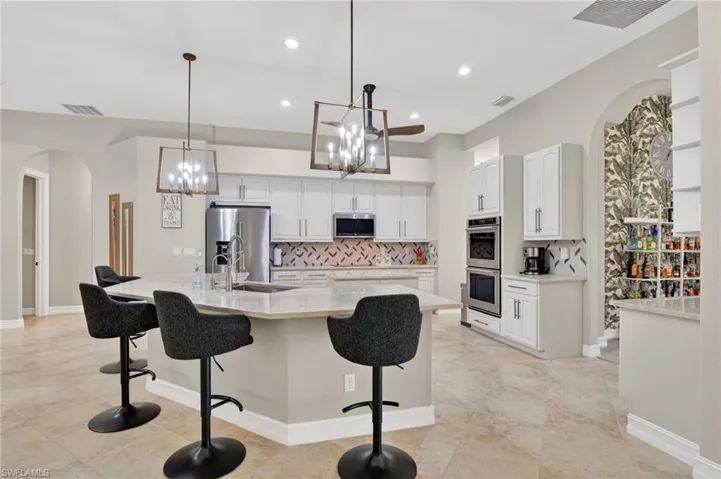 Kitchen featuring arched walkways, a kitchen bar, white cabinets, and backsplash