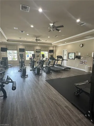 Gym featuring a tray ceiling, ornamental molding, wood-type flooring, and ceiling fan