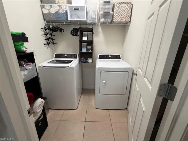 Laundry area featuring a top-load washing machine, a front-load dryer, tiled flooring, and overhead wire shelving