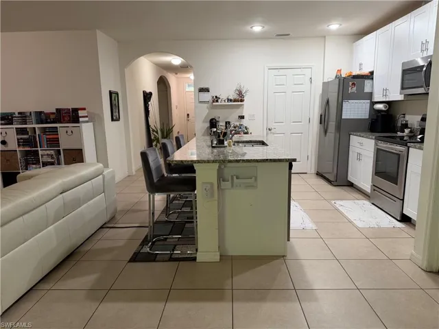 Kitchen with granite countertops, stainless steel appliances, white cabinetry, and tile flooring