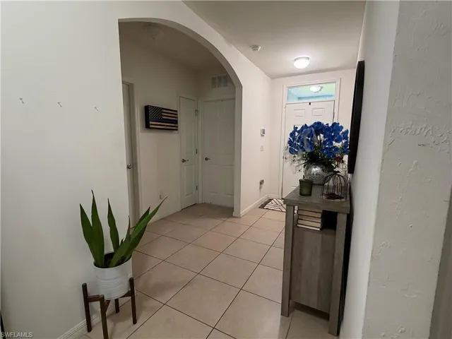 Entryway featuring neutral-toned tile flooring, an arched doorway, white interior doors, and a front entry door with a transom window