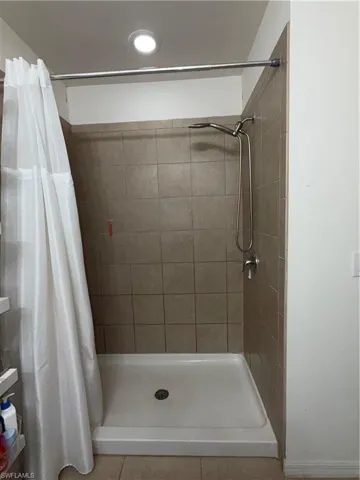 Shower stall with light-toned tiled walls, a white shower pan, and chrome fixtures