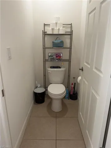 Compact powder room featuring a single toilet, neutral tile flooring, and white walls
