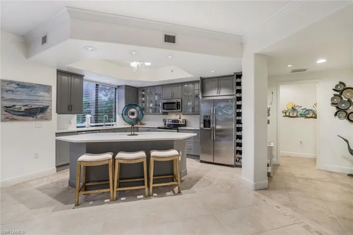 Kitchen with gray cabinets, appliances with stainless steel finishes, and a kitchen island with sink