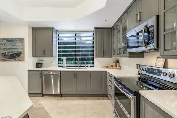 Kitchen with gray cabinetry, sink, light tile patterned flooring, a raised ceiling, and appliances with stainless steel finishes