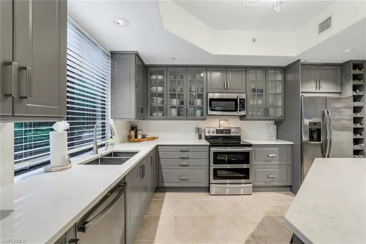 Kitchen with a raised ceiling, appliances with stainless steel finishes, sink, and gray cabinets