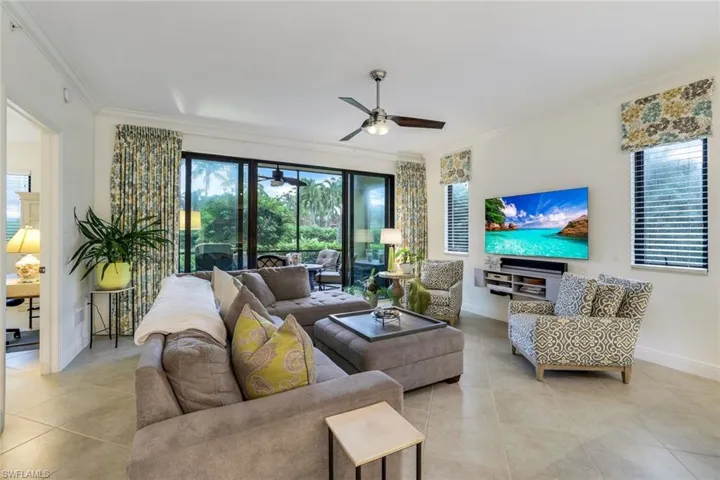 Living room with ceiling fan, ornamental molding, and light tile patterned flooring