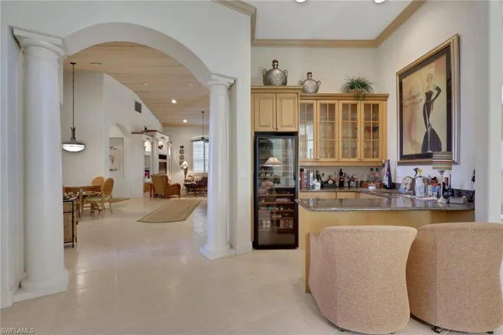 Indoor bar featuring arched walkways, light stone countertops, ornate columns, glass insert cabinets, and wine cooler