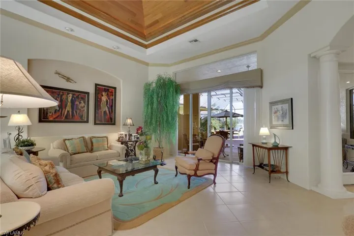 Living area with decorative columns, ornamental molding, a towering ceiling, a tray ceiling, and tile patterned floors