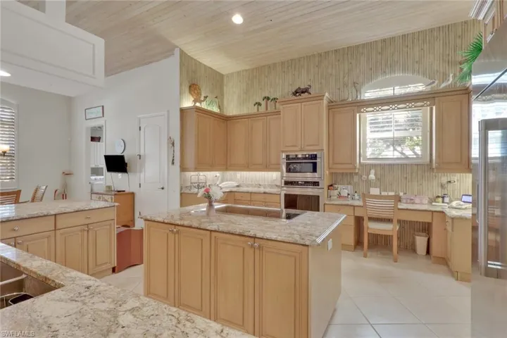Kitchen featuring light brown cabinets, stainless steel appliances, light stone countertops, light tile patterned flooring, and a center island