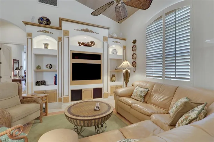 Living area with ceiling fan, built in shelves, and high vaulted ceiling