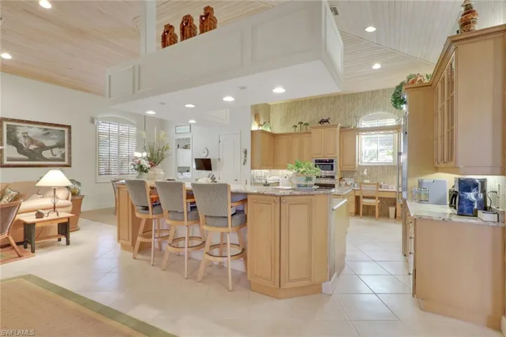 Kitchen with light brown cabinets, a breakfast bar, light stone countertops, a large island with sink, and wooden ceiling