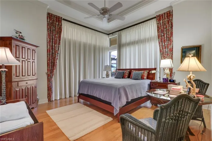 Bedroom featuring ornamental molding, light wood-style flooring, a ceiling fan, a tray ceiling, and a high ceiling