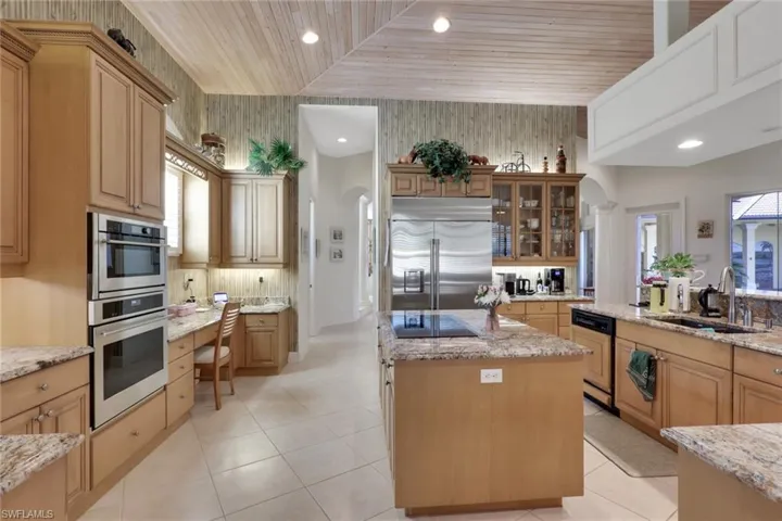 Kitchen with wooden ceiling, a kitchen island, light stone countertops, glass insert cabinets, and stainless steel appliances