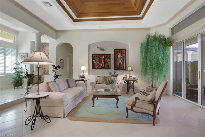 Tiled living area featuring crown molding, arched walkways, and a raised ceiling
