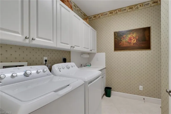 Washroom featuring wallpapered walls, cabinet space, light tile patterned flooring, and independent washer and dryer