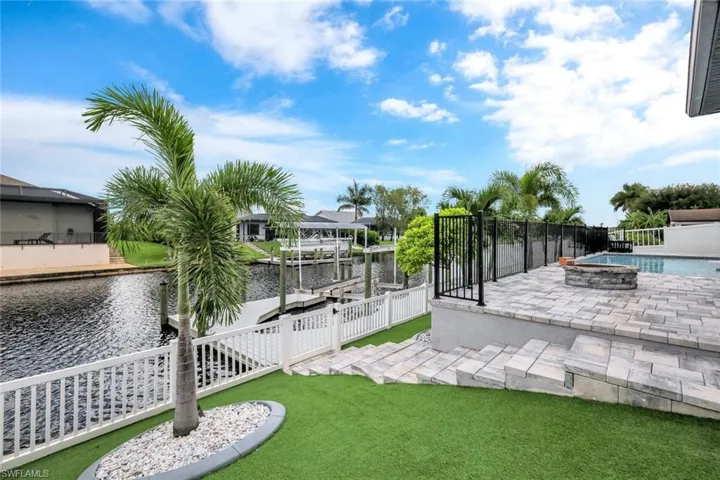 Fenced yard with artificial grass, a water view, a boat dock, and boat lift