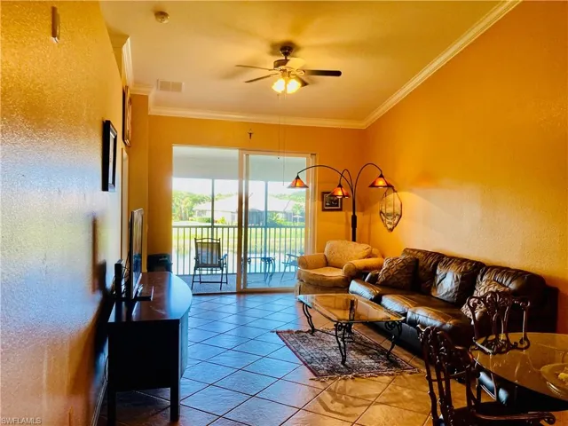 Living area featuring a textured wall, crown molding, tile patterned floors, and a ceiling fan