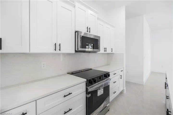 Kitchen featuring stainless steel appliances, white cabinets, light stone counters, and backsplash