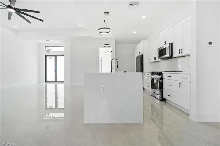 Kitchen with stainless steel appliances, hanging light fixtures, white cabinetry, a kitchen island with sink, and light stone countertops