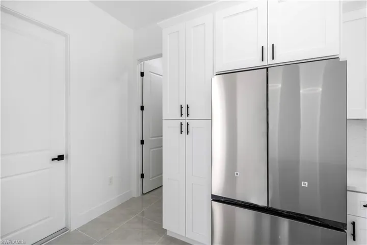 Kitchen featuring stainless steel fridge, white cabinets, light tile patterned floors, and light countertops
