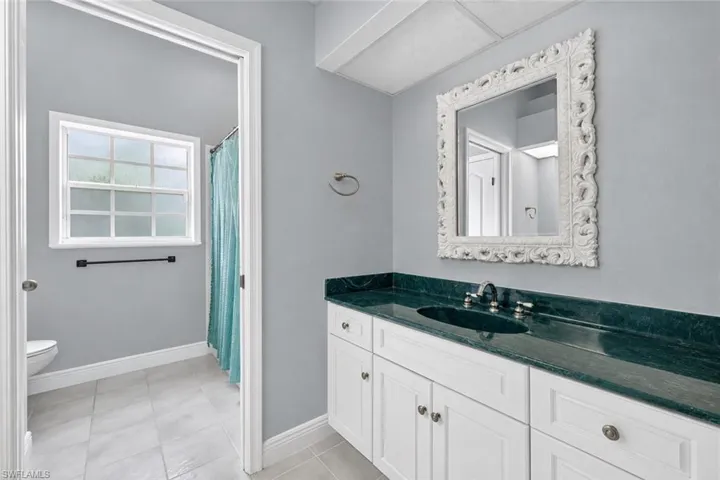 White vanity with a dark green countertop, undermount sink, and a framed mirror