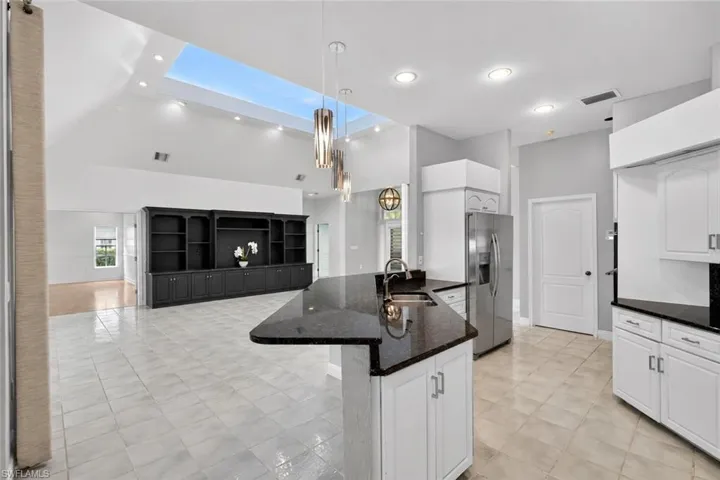 Kitchen featuring a stainless steel refrigerator, white cabinetry, dark countertops, and a skylight
