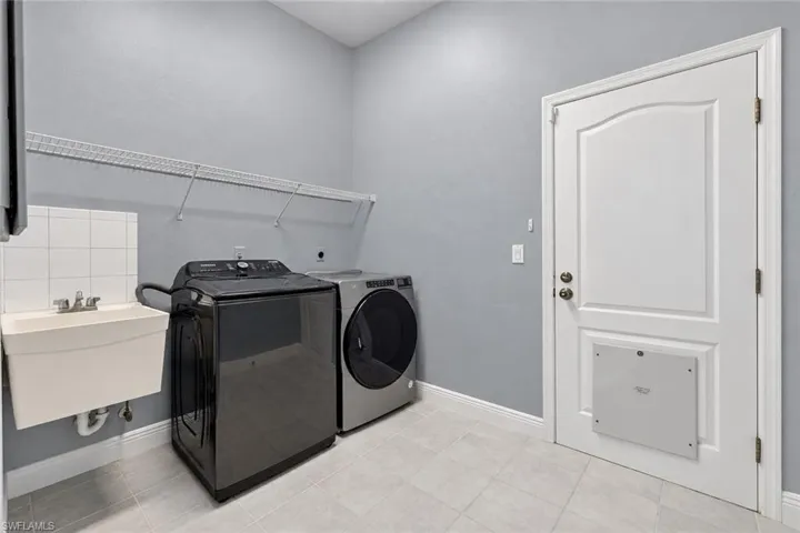 Utility sink with white tile backsplash, wire shelving, and light gray tile flooring