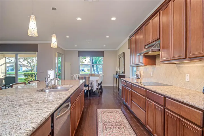 Kitchen with sink, stainless steel dishwasher, pendant lighting, black electric stovetop, and light stone countertops
