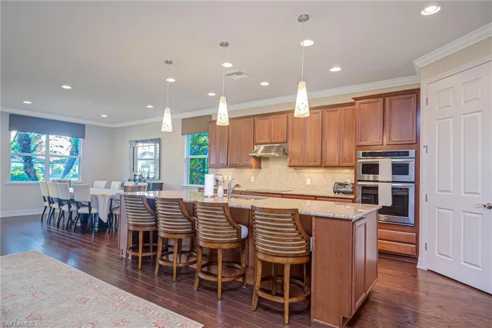 Kitchen featuring crown molding, hanging light fixtures, backsplash, a center island with sink, and stainless steel double oven