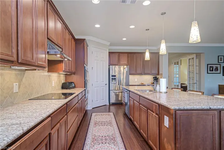 Kitchen featuring sink, hanging light fixtures, stainless steel fridge, black electric stovetop, and a kitchen island with sink