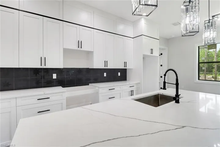 Kitchen featuring light quartz countertops,white cabinetry, decorative backsplash, and decorative light fixtures