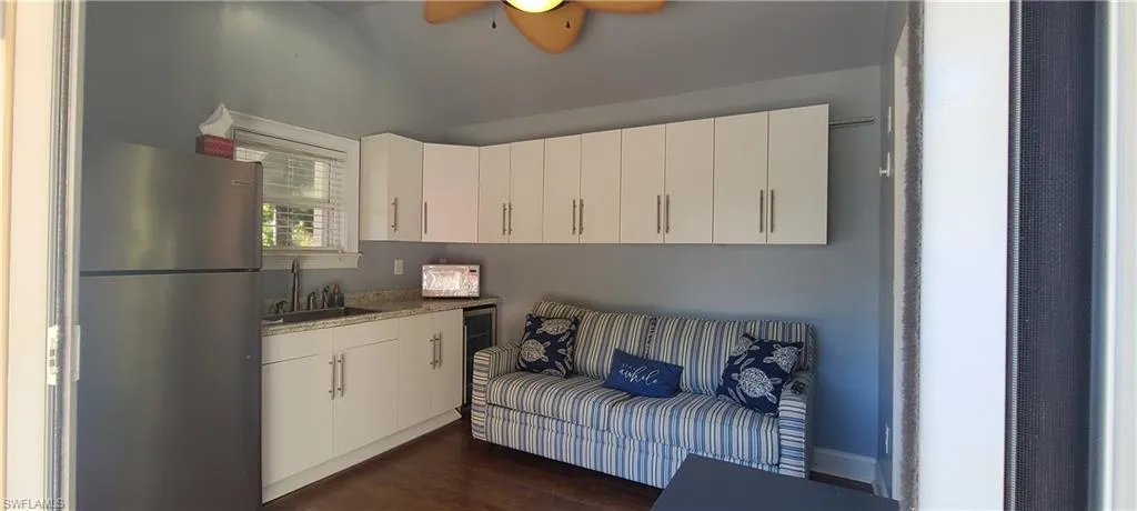 Kitchen with ceiling fan, dark wood-type flooring, sink, white cabinets, and stainless steel refrigerator