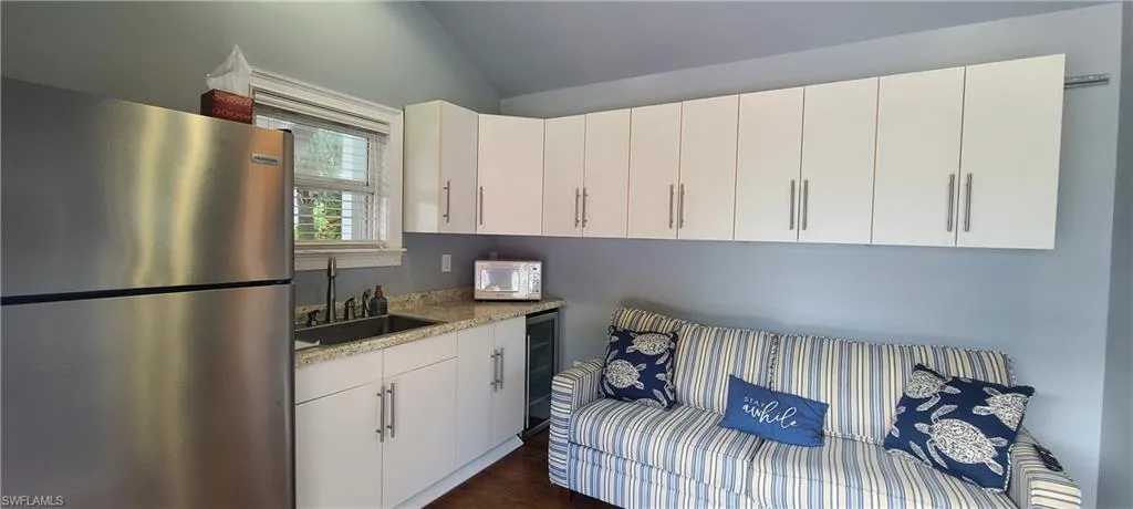 Kitchen with white cabinetry, stainless steel refrigerator, lofted ceiling, and light stone counters