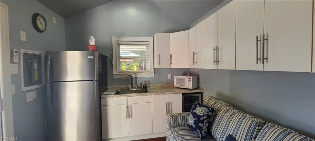 Kitchen featuring stainless steel refrigerator, sink, white cabinets, and lofted ceiling