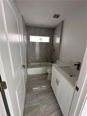 Full bathroom with tiled shower / bath, vanity, toilet, and tile floors