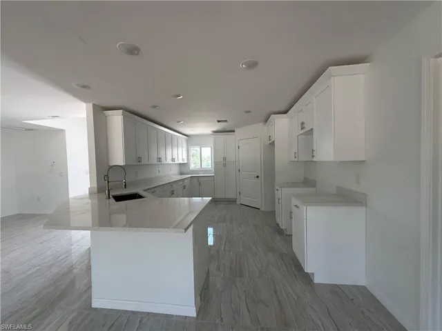 Kitchen with tile floors, white cabinets, kitchen peninsula, light stone counters, and sink