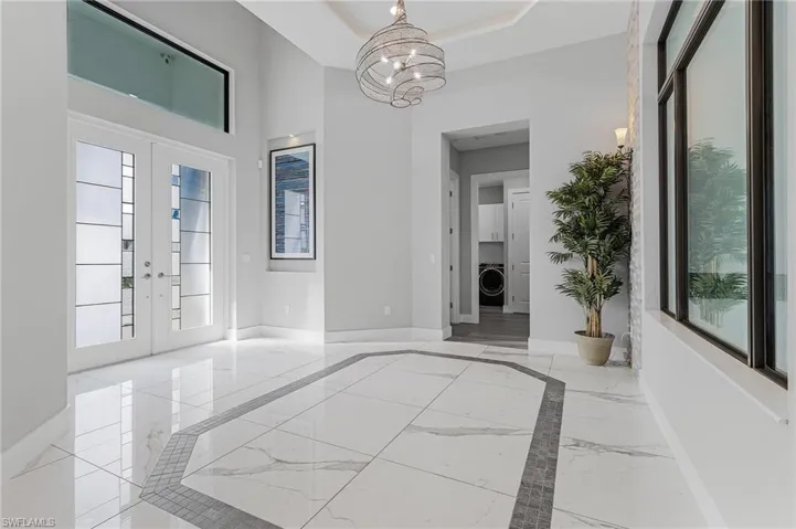 Foyer entrance featuring an inviting chandelier, washer / dryer, a tray ceiling, and french doors