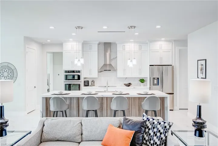 Kitchen featuring stainless steel appliances, hanging light fixtures, light tile patterned floors, and wall chimney range hood