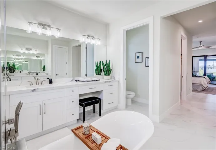Bathroom with toilet, a washtub, ceiling fan, and double vanity
