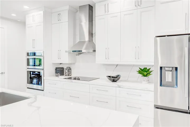 Kitchen with backsplash, white cabinets, stainless steel appliances, and wall chimney exhaust hood