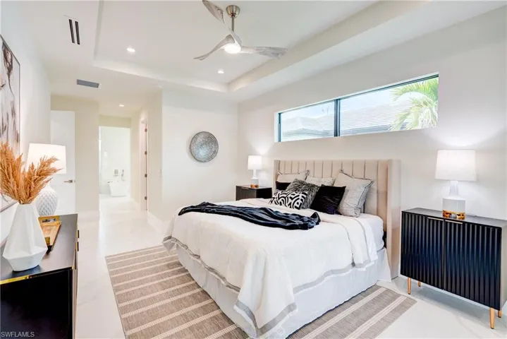 Bedroom with light tile patterned flooring, ceiling fan, a tray ceiling, and connected master bathroom, and his and hers closets.