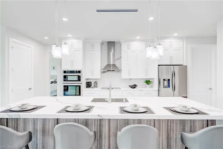 Kitchen with a breakfast bar area, stainless steel appliances, wall chimney exhaust hood, decorative light fixtures, and a spacious island.