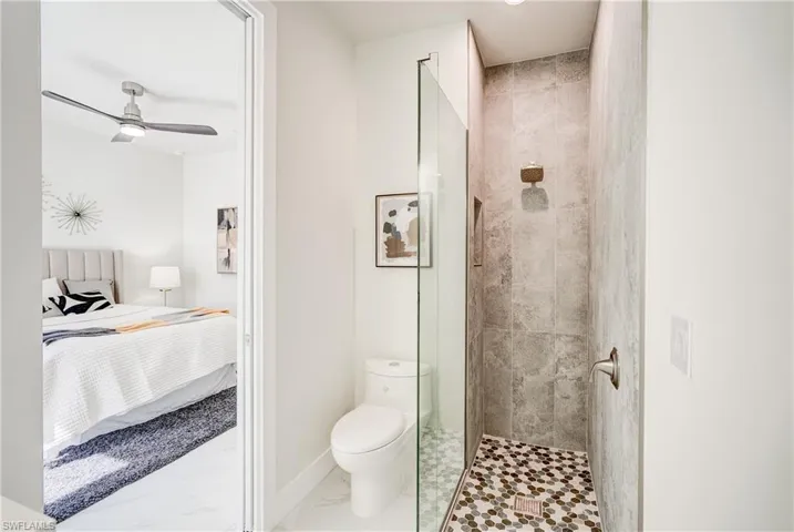 Bathroom with tile patterned floors, a shower with door, toilet, and ceiling fan