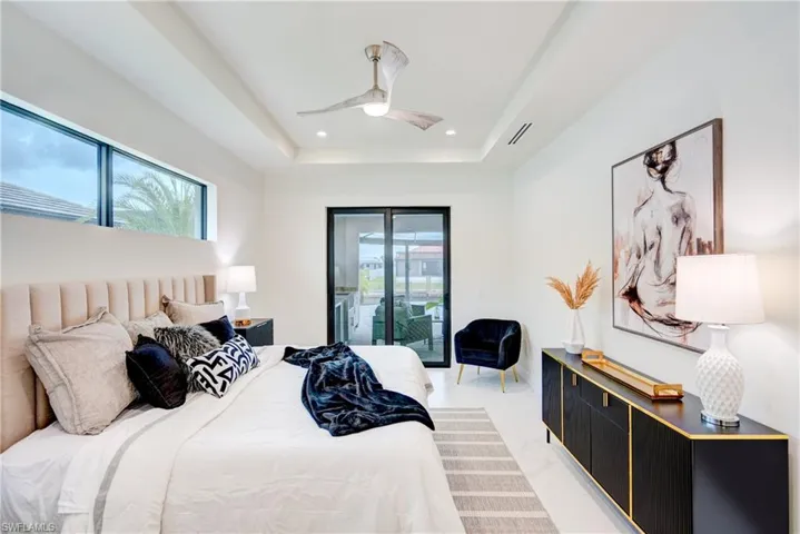 Bedroom with multiple windows, ceiling fan, a raised ceiling, and sliding door offering view to the outside.