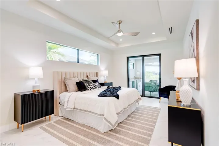 Bedroom featuring ceiling fan, access to outside, and a tray ceiling.