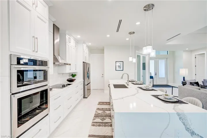 Kitchen with light tile patterned flooring, a large island, wall chimney exhaust hood, sink, and appliances with stainless steel finishes. Quartz countertops