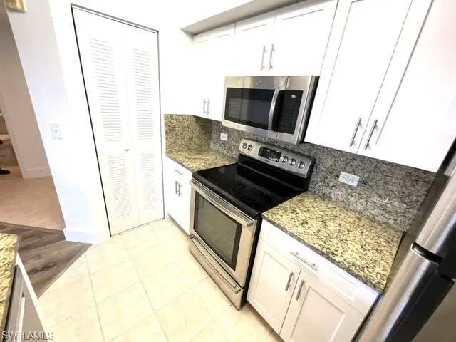 Kitchen with backsplash, appliances with stainless steel finishes, white cabinetry, and dark stone countertops