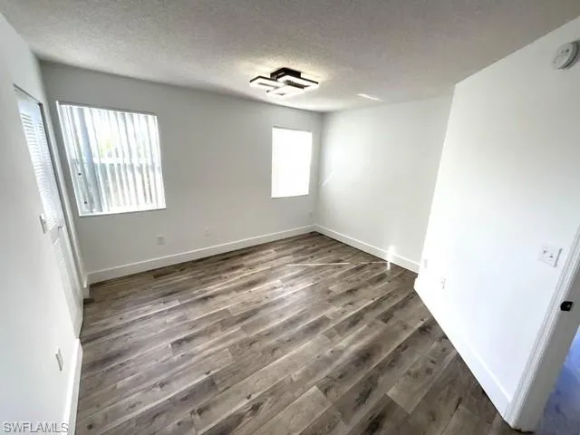 Spare room with dark wood-type flooring, a textured ceiling, and a wealth of natural light