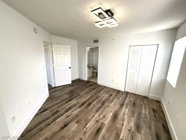 Unfurnished bedroom featuring a textured ceiling, dark hardwood / wood-style floors, a closet, and ensuite bath
